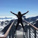 Success Stories - Person Standing on Hand Rails With Arms Wide Open Facing the Mountains and Clouds