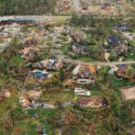Consequences - Aerial view of tornado impact on small settlement cottages with destroyed roofs windthrown trees and bent electricity transmission lines