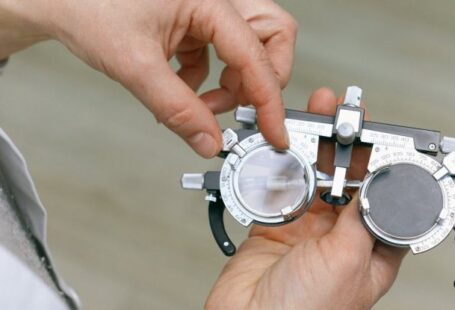 Doctorate Degree - Crop unrecognizable medic in white coat taking measuring vision glasses while adjusting scale according to numerals written on metal surface