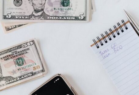 Student Loan Debt - Crop anonymous person calculating profit on smartphone calculator near banknotes