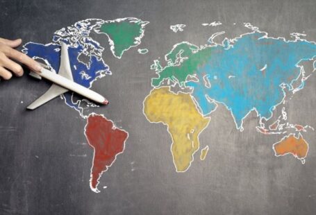 International Credentials - Top view of crop anonymous person holding toy airplane on colorful world map drawn on chalkboard