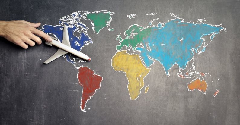International Credentials - Top view of crop anonymous person holding toy airplane on colorful world map drawn on chalkboard