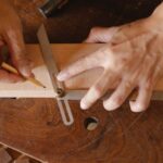 Business Degrees - High angle of skilled man using bevel tool and pencil while measuring angle of cut on workshop