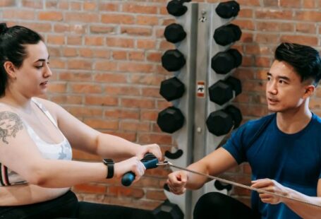 Active Recalling - Multiethnic trainer and overweight woman doing exercises with rowing machine together in sport club