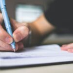 Essay Writing - Person Holding Blue Ballpoint Pen Writing in Notebook